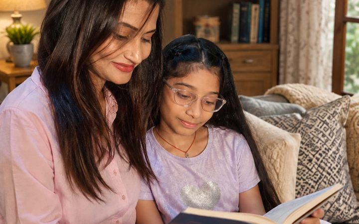 A mother and daughter sharing an open book on the sofa